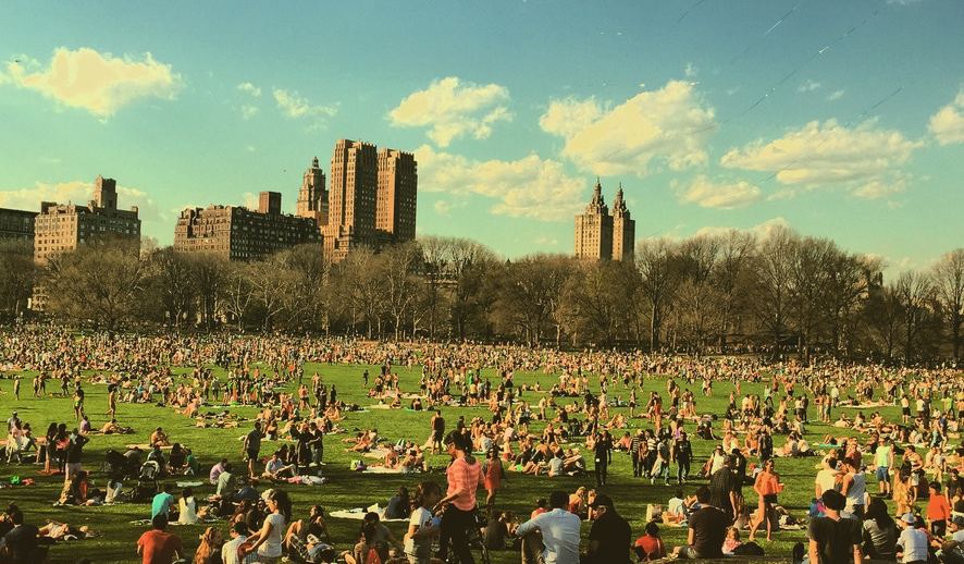 En park i New York full av folk, med høye bygårder bak